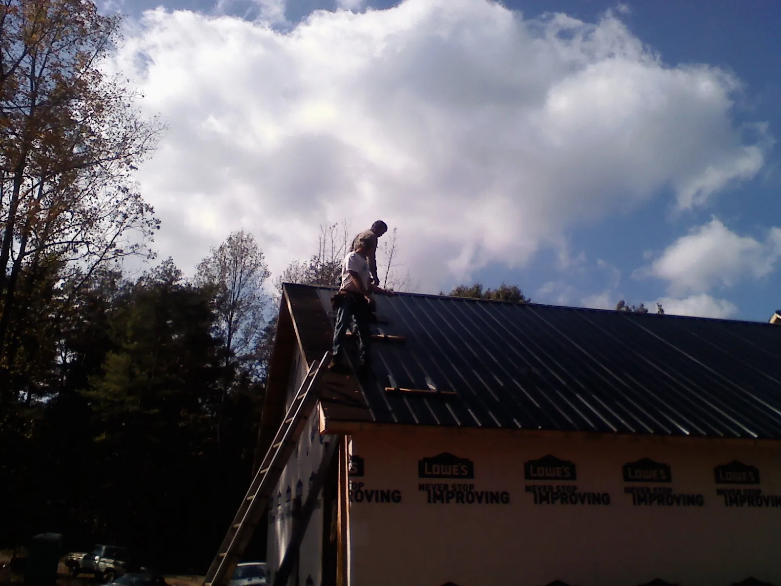 Roofer fastening dark metal panels high against a cloudy sky, from a Roof Inspection job in Hadley