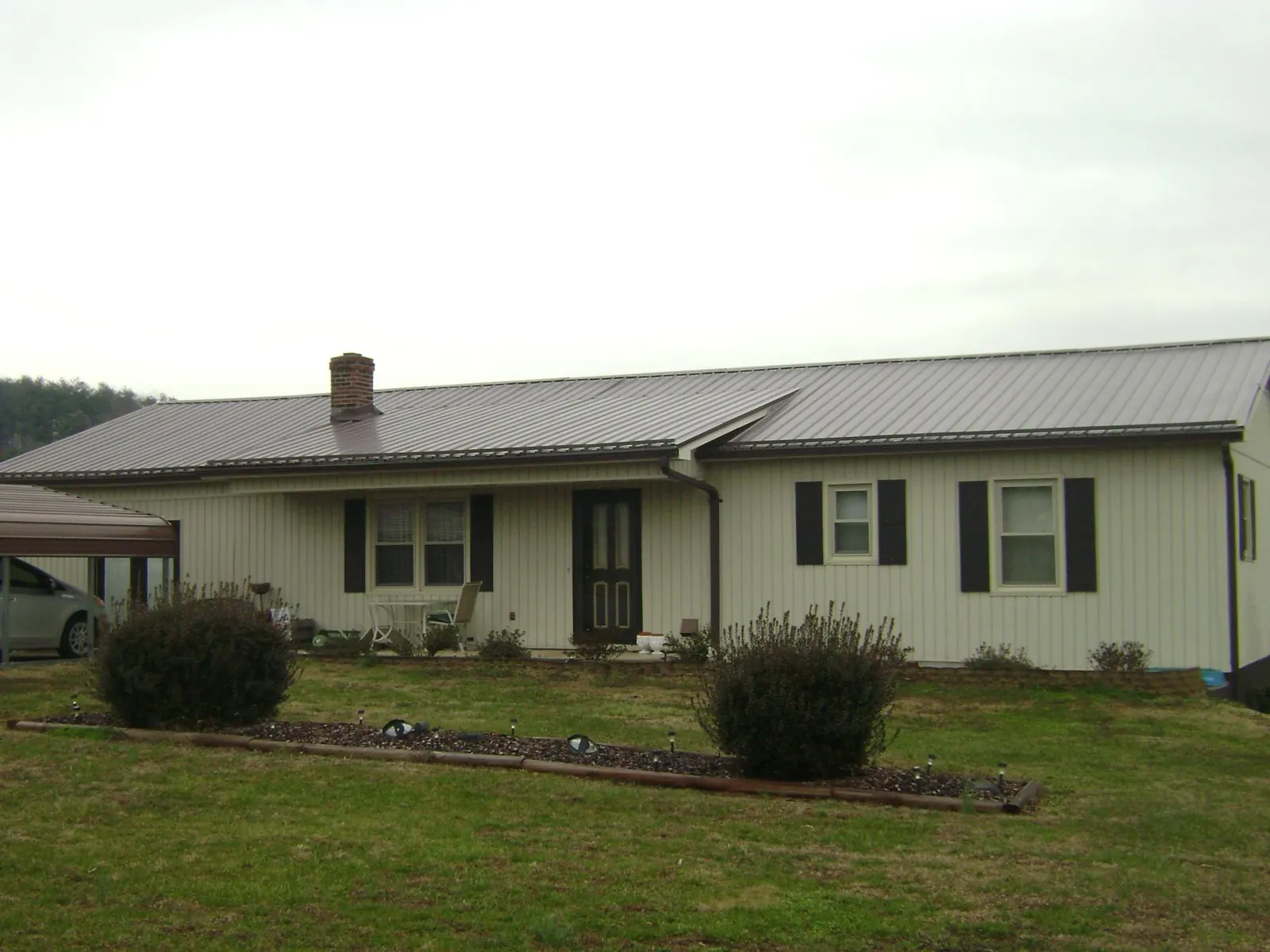 Brown metal roof on a cream sided ranch home with a brick chimney in Hadley